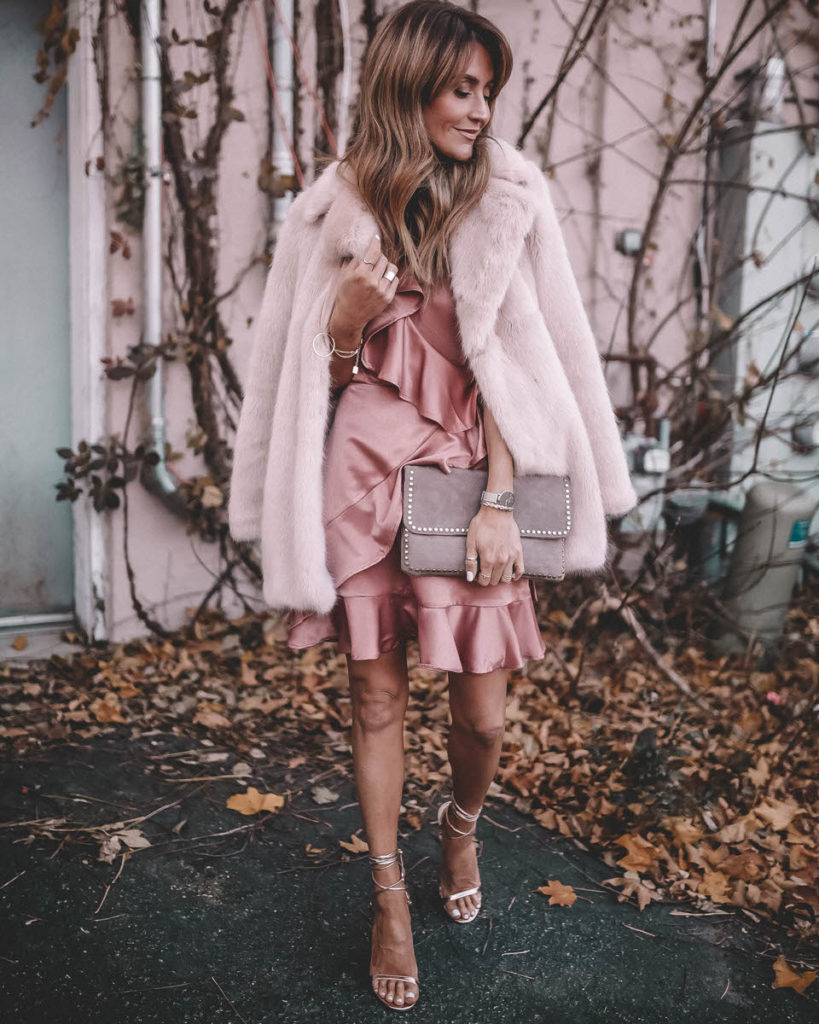 BB Dakota Limelight Pink Satin Dress Karina Reske | Hottest Pink Holiday Dress featured by top Indianapolis fashion blog, Karina Style Diaries: woman walking in the street wearing a BB Dakota pink ruffle dress, ASOS rose gold sandals, Daniel Wellington watch, grey suede clutch, gold disc necklace and a pink H&M Faux Fur coat