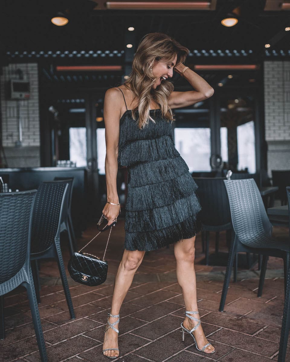 Black Fringe Dress holiday dress | Holiday Party look featured by top Indianapolis fashion blogger, Karina Style Diaries: image of a woman wearing a Lesley Jane black fringe dress, Manolo Blahnik heels, Chanel bubble bag, Daniel Wellington watch and Jemma Sands drop earrings
