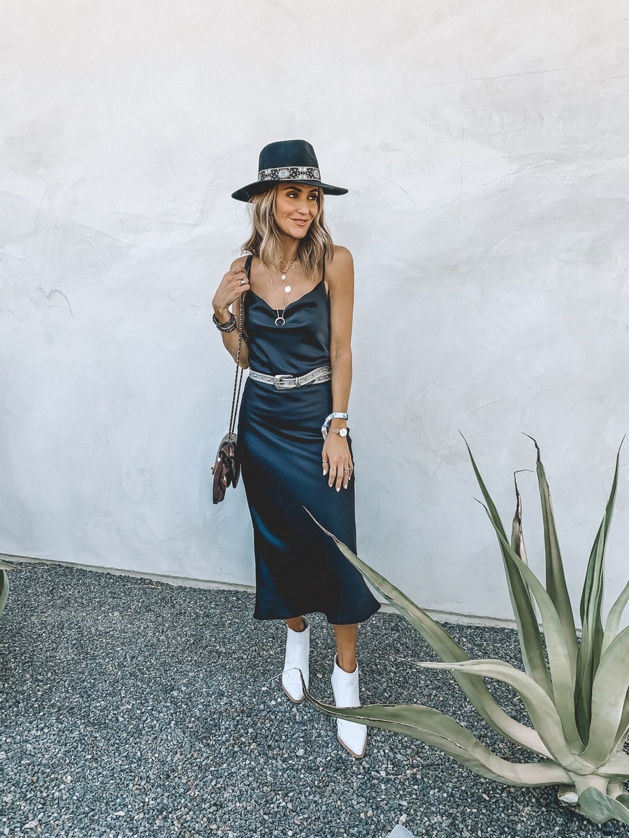 Karina Style Diaries wearing Willow and Clay black satin dress western style, metal western belt, lack of color black felt hat, white western booties, stagecoach outfit