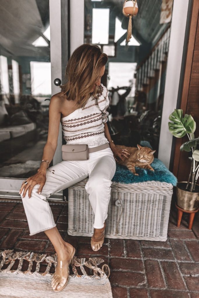 Fashion Blogger Karina Reske wearing House of Harlow one-shoulder sweater cream wide leg jeans clear heels belt bag sunroom outfit