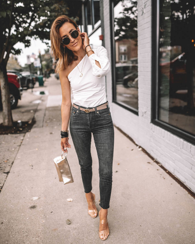 Karina Style Diaries wearing one-shoulder trend Revolve white top Levi's wedgie high waist black jeans clear heels Gucci Belt outfit