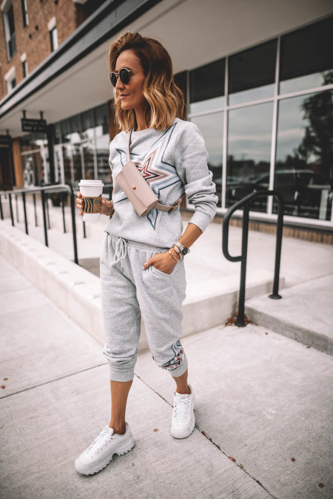 Karina Style Diaries standing having coffee wearing grey star swetshirt pant set white sneakers pink belt bag across the chest