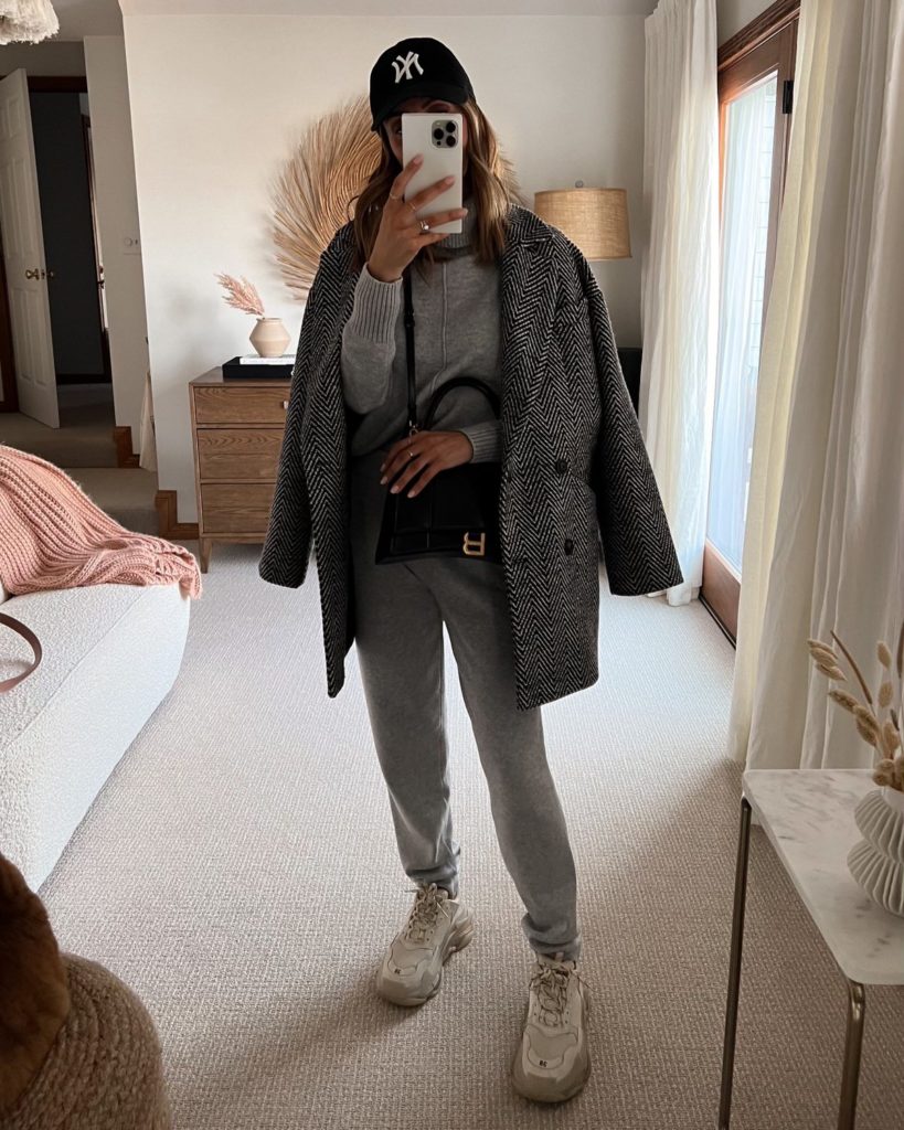 Karina wears grey amazon sweater set with wool coat and sneakers and ball cap
