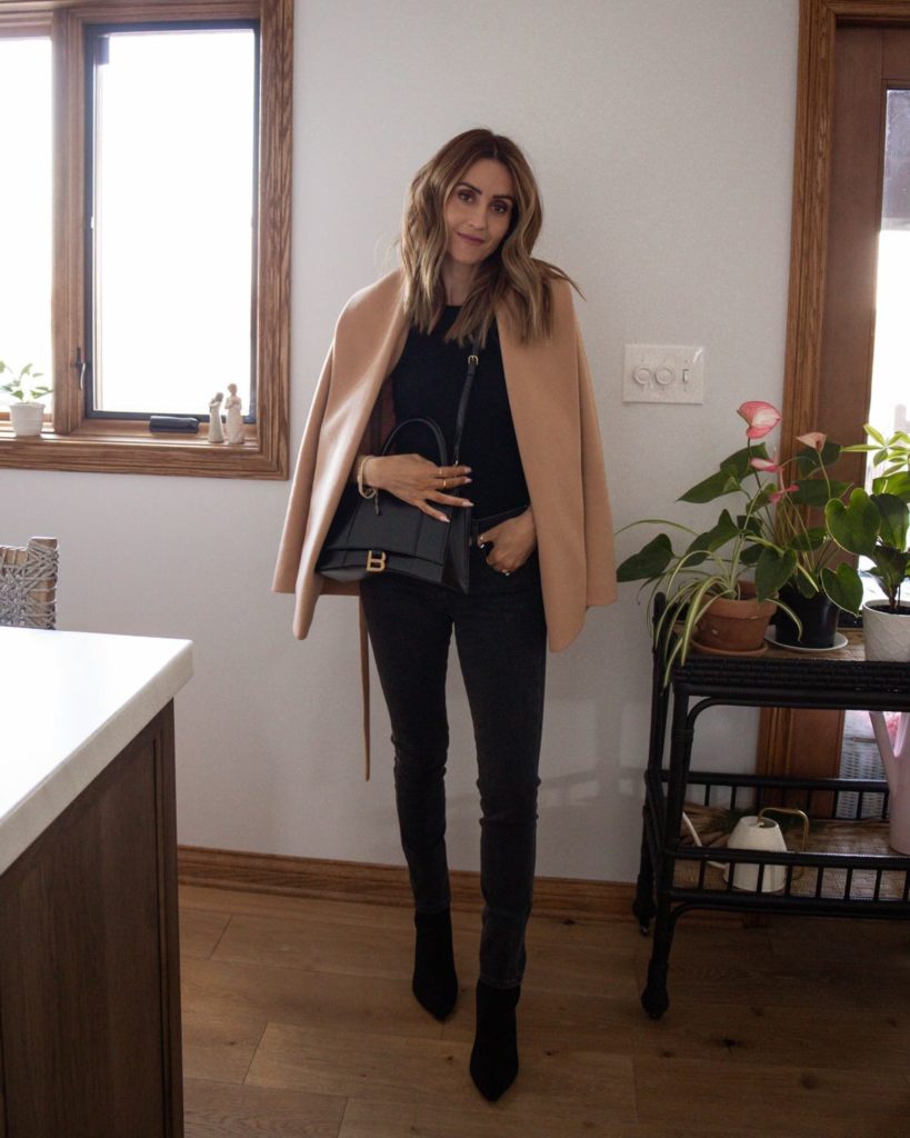 Karina wears express camel wrap coat with black sweater tank and black jeans and balenciaga bag