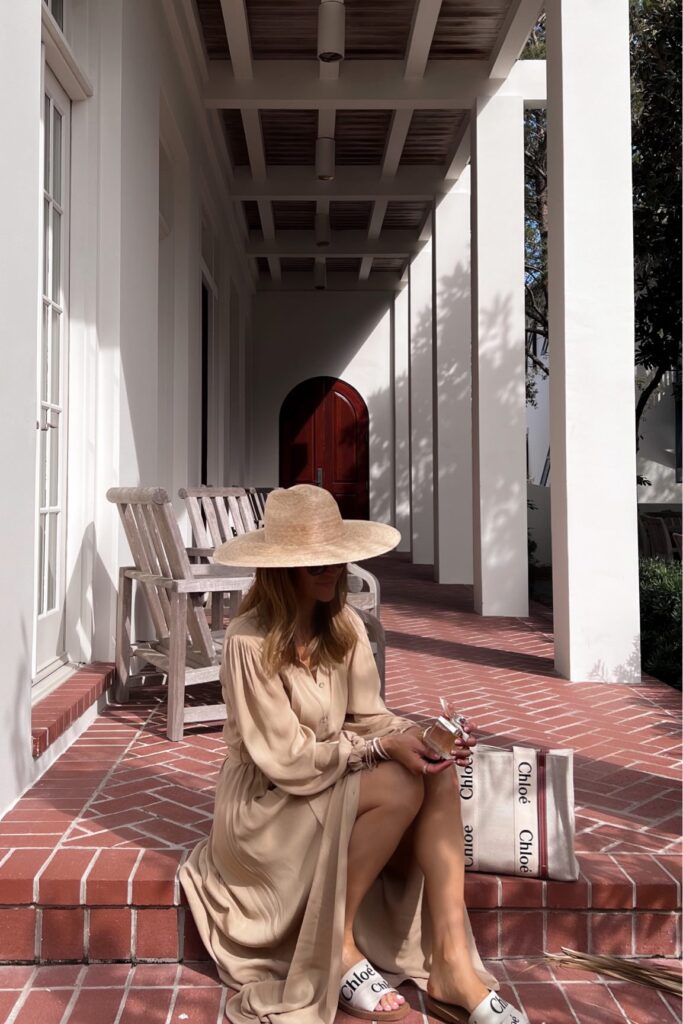 karina wears chloe fragrance and chloe tote bag and slide sandals with tan dress and sunhat