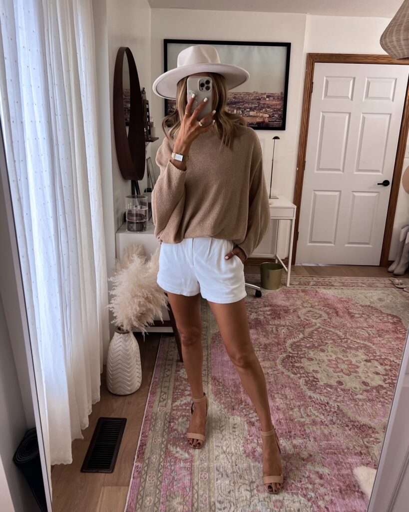 Karina wears pink lily pullover sweater with linen shorts and wide brim fedora