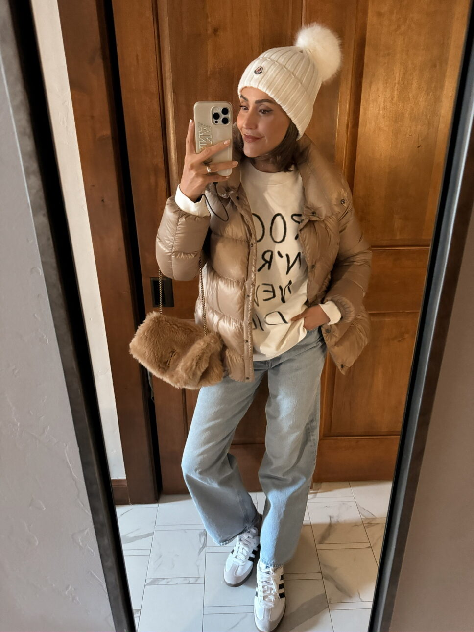 casual ski trip outfit with denim, a sweatshirt, a puffer jacket, adidas samba sneakers, and a shearling purse