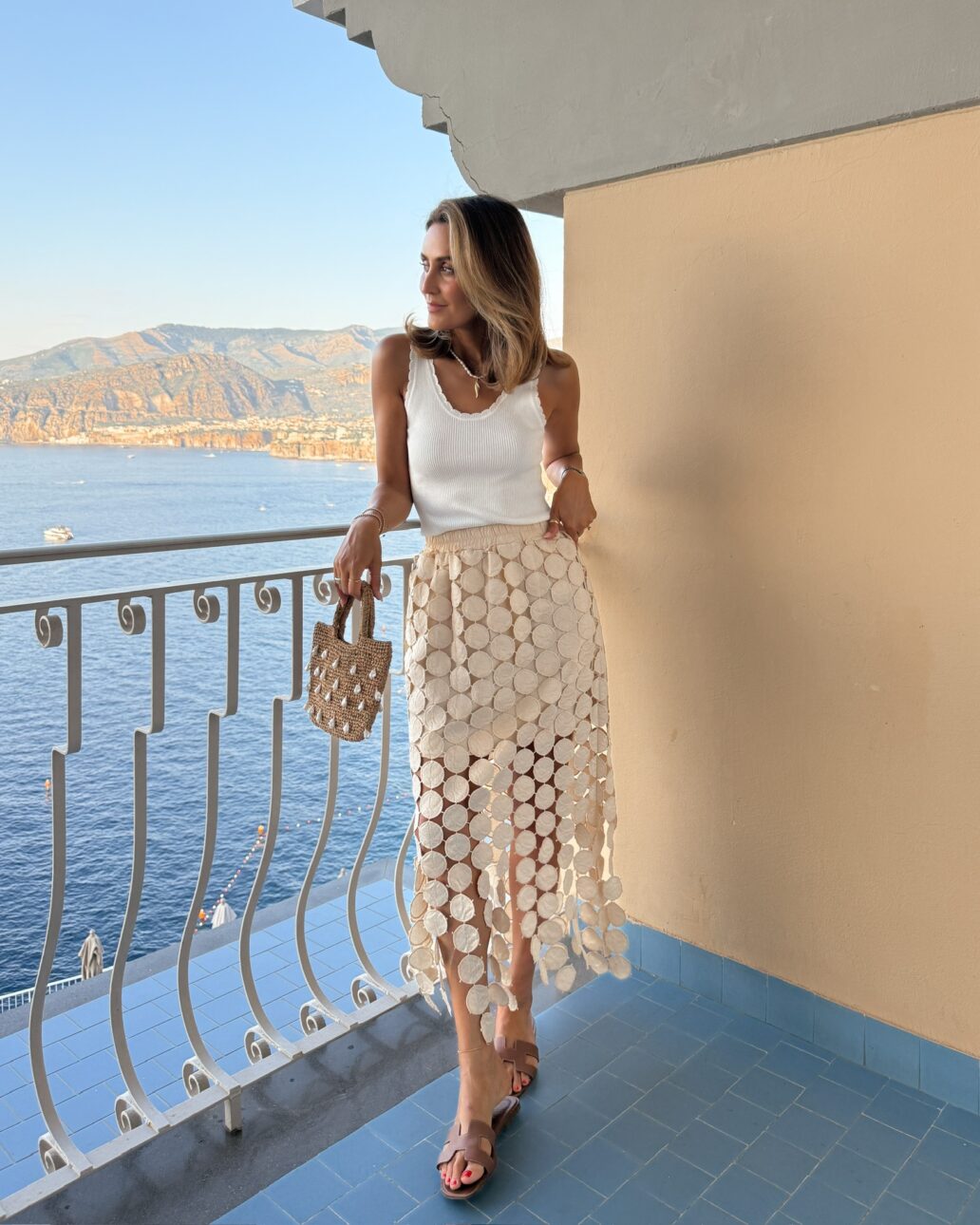 Amazon statement skirt, scalloped white knit tank, Hermes slide flats shell raffia evening bag.
